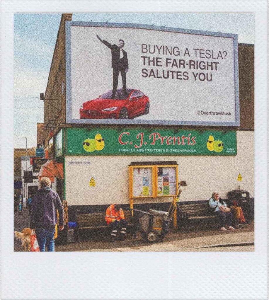 Un cartellone pubblicitario affisso nella cittadina Broadstairs nel Kent in cui si vede Elon Musk in piedi sul cofano di una Tesla che fa il saluto romano. Il testo recita "Buynig a Tesla? The Far-Right salutes you". Firmato @OverthrowMusk